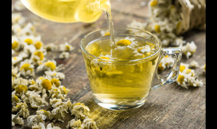 glass-cup-of-chamomile-tea with flowers and teapot-on-rustic-wooden-background