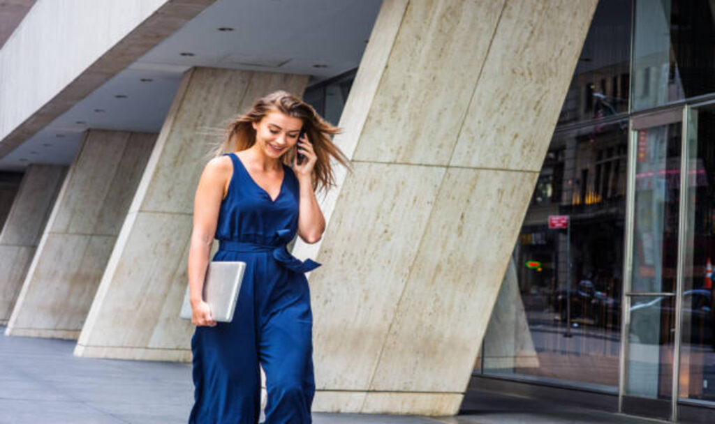 Women in jumpsuit holding laptop and using phone