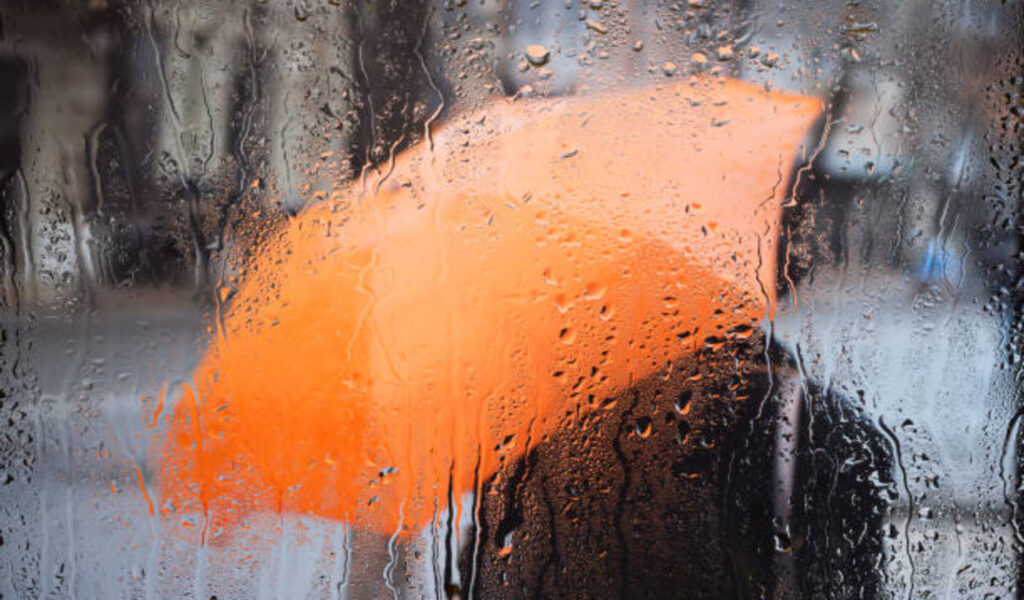 Raindrops on glass and person holding umbrella