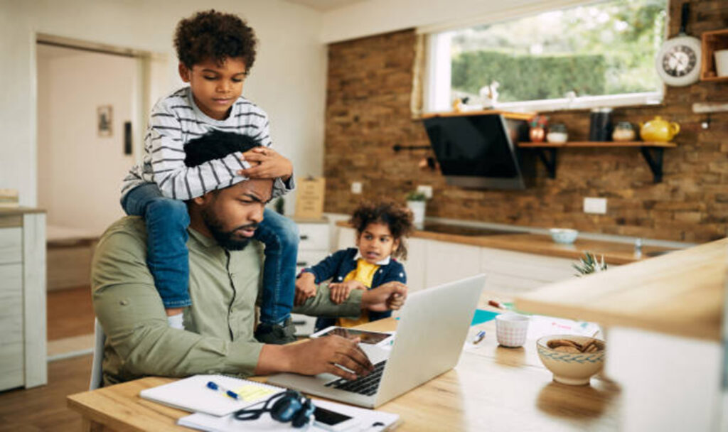 Father working on laptop and children seeking his attention