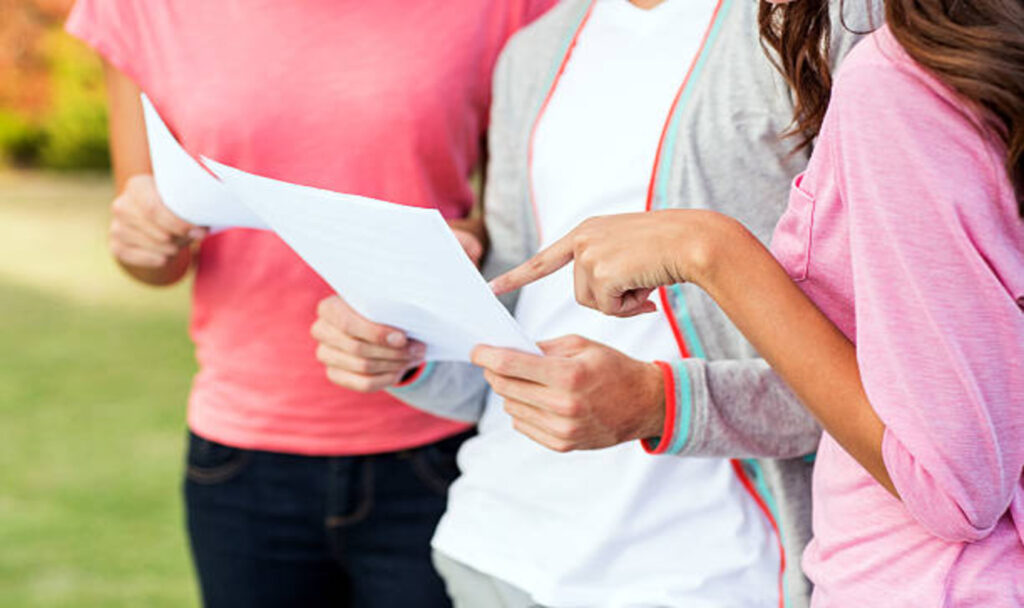 Girl pointing-at-paper standing with friends