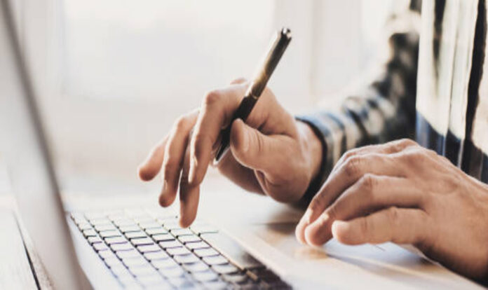 Hands using laptop and holding pen